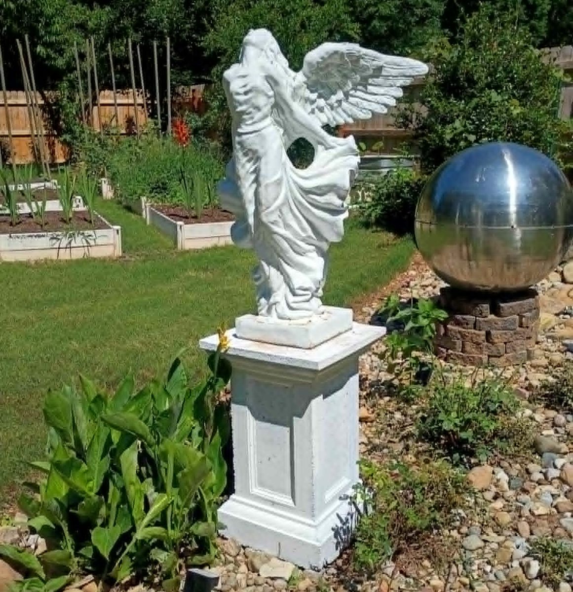 A winged angel statue on a pedestal in a landscaped garden