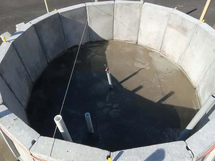 Fresh concrete poured over the rebar inside the round fountain basin, plumbing stubs standing