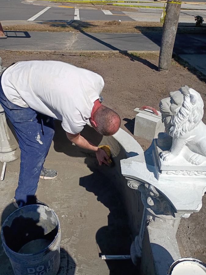Chris hand-finishing a cast concrete piece beside a lion statue in the yard