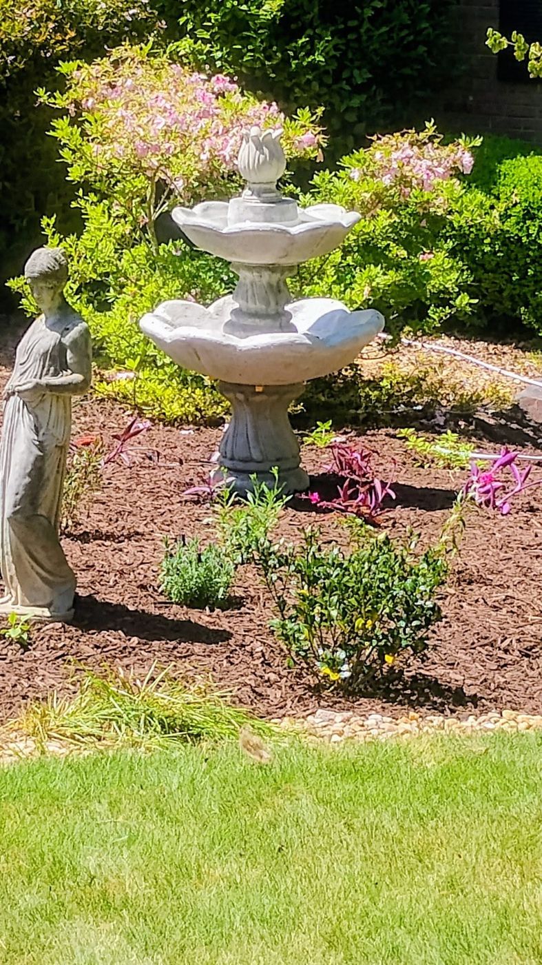 Two-tier garden fountain installed beside a lady statue in a flower bed
