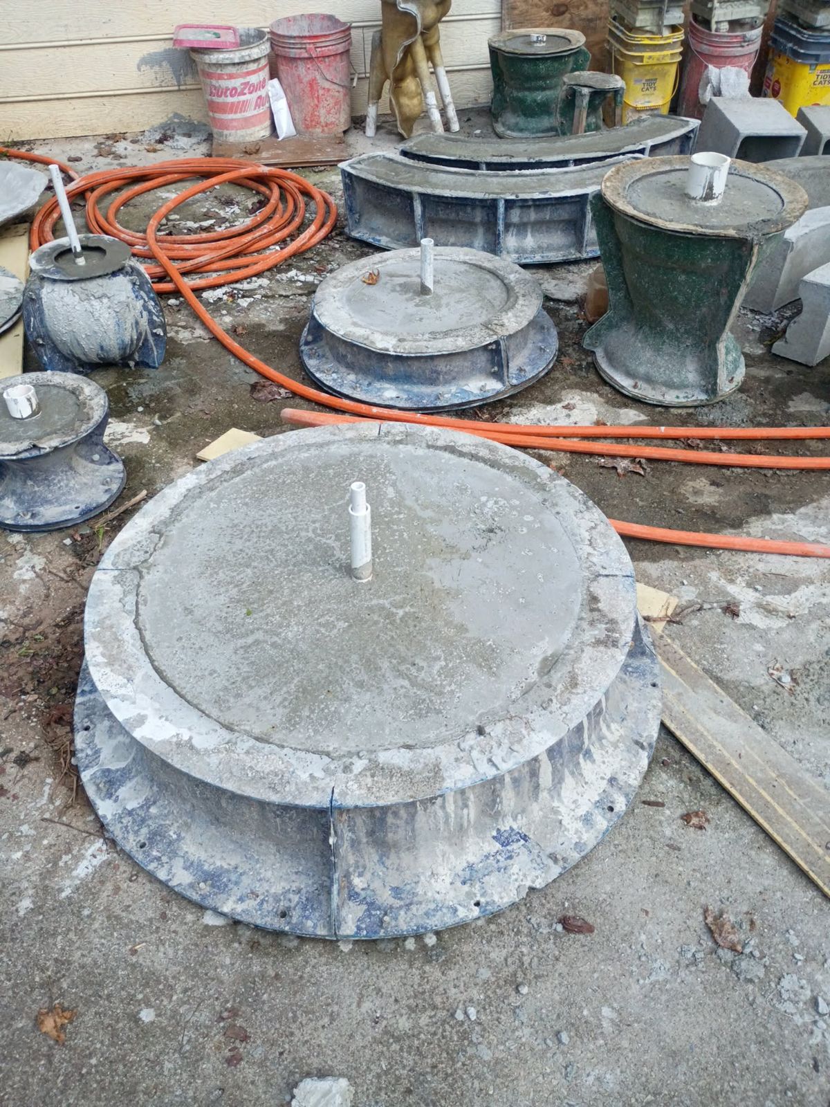 Concrete tier bowls and pedestal pieces for The Majestic curing in their molds with PVC pump lines in place