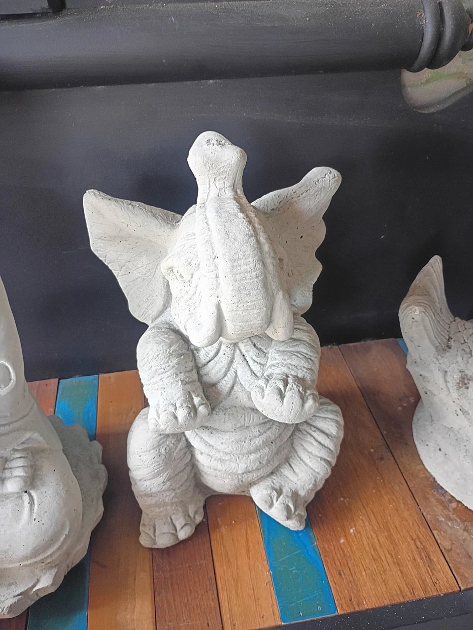 Concrete baby elephant statue with its trunk raised, natural gray, on display at Red Door Antiques in LaGrange, GA